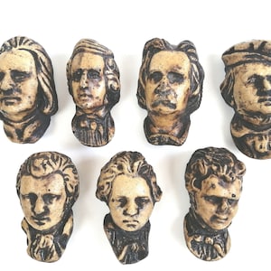 May include: Seven ceramic busts of famous composers, each with a unique hairstyle and facial expression. The busts are painted in shades of brown and beige, with details in black.