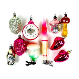 Puede incluir: Una colección de adornos navideños vintage en varias formas, incluyendo un reloj, setas y una piña. Los adornos presentan una variedad de colores, incluyendo rosa, rojo, plateado y amarillo. Cada adorno tiene una tapa de metal para colgar.
