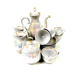 May include: A pearlescent tea set with gold trim, including a teapot, sugar bowl, creamer, cups, and saucers. The set has an iridescent finish that reflects multiple colours. The tea set is arranged on a white background.