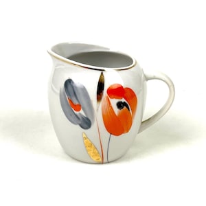 Può includere: Lattiera in ceramica bianca con bordo e manico dorati. La lattiera è decorata con motivi floreali arancioni e grigi stilizzati e accenti in foglia d'oro. Un pezzo vintage.