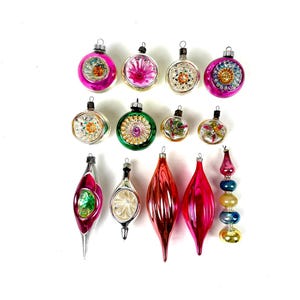 Puede incluir: Una colección de adornos navideños vintage de varias formas y colores. Los adornos incluyen formas redondas, de lágrima y de carámbano, con colores como rosa, rojo, verde y plateado. Algunos adornos tienen diseños florales o de estrella.