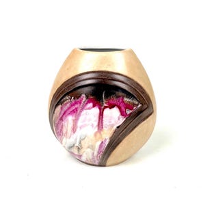 May include: A handcrafted, decorative vase with a unique design. The vase features a light tan exterior with a dark brown, geometric accent. The focal point is a vibrant, abstract design in shades of pink, white, and black.