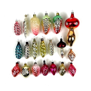 Puede incluir: Una colección de adornos navideños vintage de varias formas y colores. Los adornos incluyen gotas, espirales y diseños bulbosos en rojo, rosa, verde, dorado y plateado. Algunos tienen superficies texturizadas y acabados metálicos.