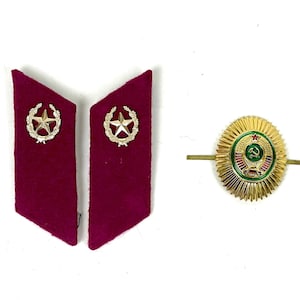 May include: Two maroon felt collar tabs, each featuring a silver-toned star emblem surrounded by a wreath, alongside a gold-toned oval badge with a green center, a red star, and a hammer and sickle symbol with radiating sunburst edges.