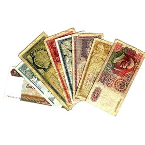 Può includere: Una collezione di banconote vintage a ventaglio su sfondo bianco. Le banconote presentano vari colori, tra cui verde, rosso e giallo, con disegni e testi intricati. Le denominazioni e le origini delle banconote non sono visibili.