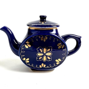 Könnte beinhalten: Eine marineblaue Keramik-Teekanne mit Deckel und Henkel. Die Teekanne hat goldene Blumendesigns und Verzierungen. Die Teekanne ist ein dekorativer Artikel zum Servieren von Tee.