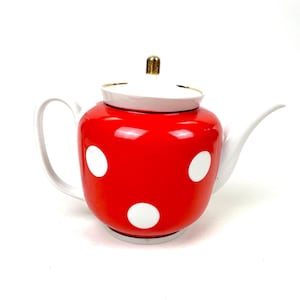 Op de afbeelding: Rode keramische theepot met witte stippen. De theepot heeft een wit handvat en tuit, en een wit deksel met een goudkleurige knop. Klassiek ontwerp.