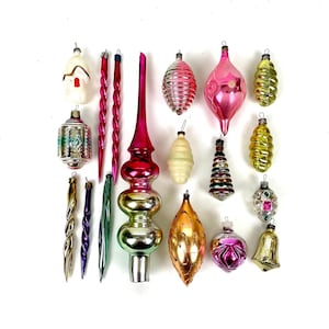 May include: A collection of vintage glass Christmas ornaments in various shapes and colors, including a large central tree topper, long twisted icicles, ribbed spheres, and teardrop designs in shades of pink, gold, green, silver, and white.