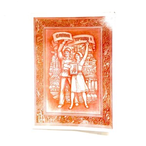 May include: A vintage postcard with a red-orange illustration. It depicts a man and woman holding a banner with Cyrillic text, standing in front of a cityscape. The postcard has an ornate border.