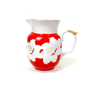 May include: A white ceramic mug with a black handle and the text "But First, Coffee" in a bold, black font. The mug is set against a blurred background, highlighting its clean design.