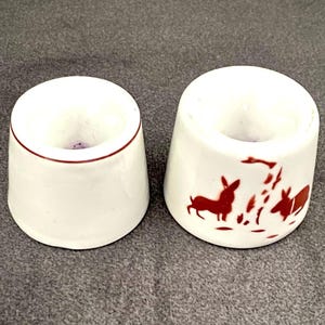 Puede incluir: Una taza de cerámica blanca con un asa negra y el texto "But First, Coffee" en negrita negra. La taza se encuentra sobre un fondo borroso, resaltando su diseño simple.