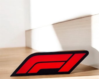 Può includere: Un logo di Formula 1 rosso e nero in legno. Il logo è su una superficie in legno chiaro.