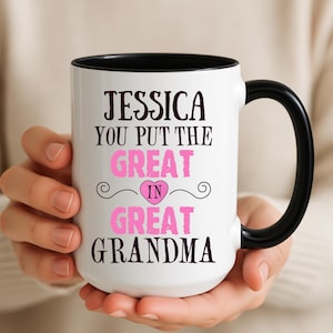 Peut inclure: Mug en céramique blanche avec une anse et un bord noirs. Le mug présente le texte "JESSICA YOU PUT THE GREAT IN GREAT GRANDMA" en lettres noires et roses. Un cœur rose est dans le mot "GREAT".