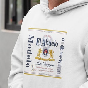 Op de afbeelding: Witte hoodie met een afbeelding van een Modelo-bierblik met de tekst "El Abuelo" en "Mas Chingon".