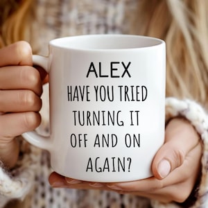 Puede incluir: Taza de cerámica blanca con el nombre "ALEX" y el texto "HAVE YOU TRIED TURNING IT OFF AND ON AGAIN?" impreso en negro. La taza tiene un asa curva y la sostiene una persona.