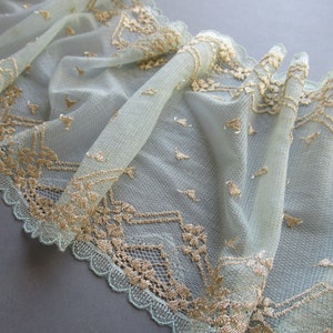 May include: Pale blue lace trim with a gold embroidered pattern. The lace has a scalloped edge.