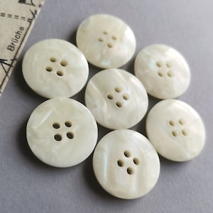 May include: Seven white pearl buttons with four holes each. The buttons have a slightly iridescent finish.