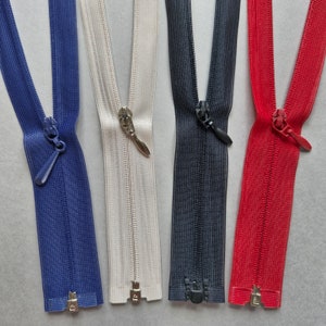 Può includere: Quattro nastri di cerniera lampo in diversi colori: blu, bianco, nero e rosso. Le cerniere sono aperte e i cursori sono visibili.