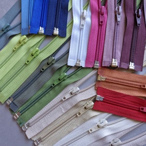 May include: A collection of colorful zippers in various shades, including blue, green, pink, and brown. The zippers are arranged in a scattered pattern, showcasing their different colors and styles. Each zipper has a metal slider and teeth.