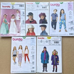 May include: Five Burda sewing pattern envelopes for children's clothing. The collection includes patterns for dresses, various hats, trousers, and coats, each featuring illustrations of children wearing the finished garments and technical line drawings.