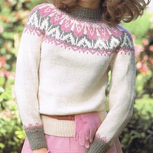 Könnte beinhalten: Cremefarbener Strickpullover mit einem gemusterten Passe in Rosa und Grau. Der Pullover hat lange Ärmel und einen gerippten Kragen und Bündchen. Ein rosa Handschuh ist im Bund eines rosa Rocks verstaut.