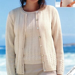 May include: A cream-colored, knitted cardigan and matching top set. The cardigan has a button-up front and long sleeves. The top is sleeveless. Both pieces feature a delicate, open-knit design. The set is made of a soft, light-colored yarn, perfect for layering.