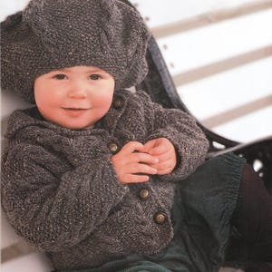 May include: A baby wearing a gray knit hat and matching button-up sweater. The sweater has four decorative buttons. The baby is also wearing dark green corduroy pants. The outfit is a cozy, handmade style.