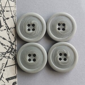 May include: Four gray plastic buttons with four holes each. The buttons have a swirl pattern.