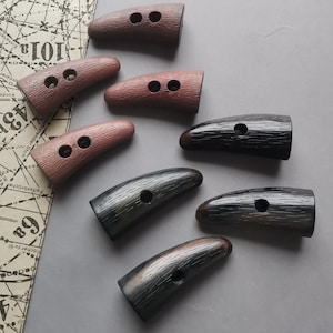 Puede incluir: Siete botones en forma de cuerno con dos agujeros cada uno. Los botones están hechos de un material marrón oscuro, marrón claro y negro. Los botones tienen una superficie texturizada.