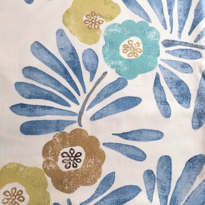 May include: Close-up of a white fabric with a repeating floral pattern. The design features stylized flowers in shades of teal, gold, and brown, with blue leaf-like shapes. The overall aesthetic is reminiscent of a vintage or botanical print.
