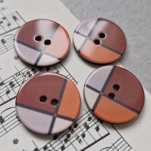 Könnte beinhalten: Vier runde, zweilöcherige Knöpfe mit einem geometrischen Muster in Braun-, Orange- und Grautönen.