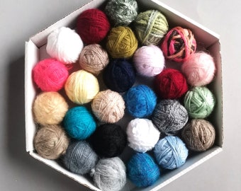 May include: A collection of colorful yarn balls in various shades of pink, red, blue, green, yellow, white, and brown. The yarn balls are arranged in a hexagonal pattern on a white surface.