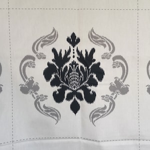 Può includere: Tessuto color crema con un motivo ripetuto di un motivo floreale damascato nero. Il damasco è centrato all'interno di una griglia di linee grigio chiaro. Elementi stilizzati di foglie e volute grigie circondano il motivo floreale centrale.