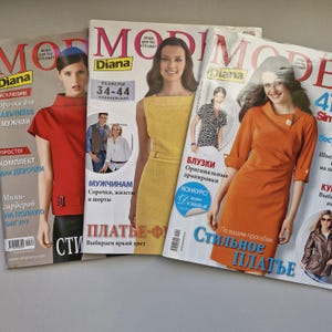 Könnte beinhalten: Drei Modemagazine mit dem Titel "Mode Diana" auf dem Cover. Die Magazine zeigen verschiedene Models in unterschiedlichen Kleidungsstilen. Der Text auf den Covern umfasst "Größen 34-44", "Herrenhemden, Westen und Shorts", "Kleider", "Blusen", "Stilvolles Kleid" und "Wettbewerb".
