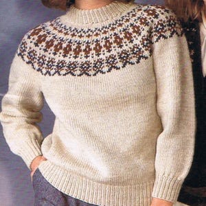 May include: A beige knit sweater with a high neckline and long sleeves. The yoke features a geometric pattern in shades of brown and black. The sweater has ribbed cuffs and hem.