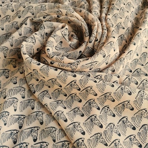 Pode incluir: Um tecido bege com estampa de zebra preta. O tecido está reunido e dobrado para mostrar o padrão.