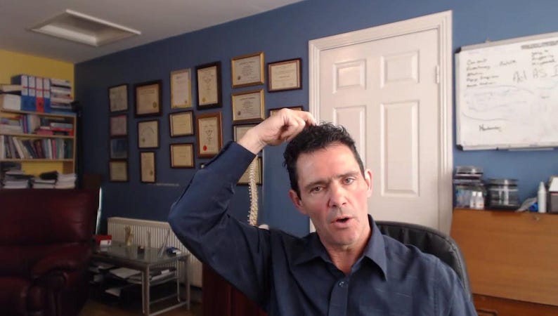 Peut inclure: Un homme aux cheveux fonc&eacute;s porte une chemise bleue et se tient dans un bureau. Il regarde la cam&eacute;ra et a la main sur la t&ecirc;te. Il y a des certificats encadr&eacute;s au mur derri&egrave;re lui.