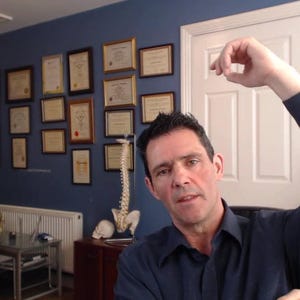 Peut inclure: Un homme portant une chemise bleue se tient dans un bureau avec un mur bleu. Il l&egrave;ve son bras droit au-dessus de sa t&ecirc;te. Il y a des certificats encadr&eacute;s sur le mur derri&egrave;re lui.