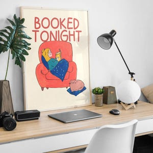 Puede incluir: Ilustraci&oacute;n enmarcada con el texto "BOOKED TONIGHT" que representa a una persona leyendo en un sill&oacute;n rojo, sosteniendo una bebida. Un gato rosa descansa sobre un coj&iacute;n azul. La escena se desarrolla en un escritorio de madera con un port&aacute;til, una l&aacute;mpara y accesorios.