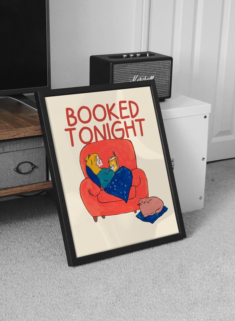 Puede incluir: L&aacute;mina art&iacute;stica enmarcada con el texto "BOOKED TONIGHT" en rojo. La ilustraci&oacute;n representa a una persona leyendo en un sill&oacute;n rojo, cubierta con una manta azul, y un gato descansando sobre un coj&iacute;n azul.