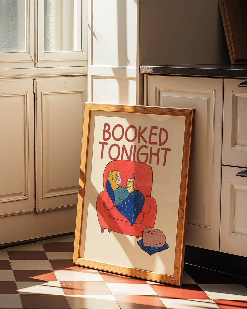Puede incluir: Una impresi&oacute;n art&iacute;stica enmarcada con las palabras "BOOKED TONIGHT" en rojo. La ilustraci&oacute;n representa a una persona leyendo en un sill&oacute;n rojo, cubierta con una manta azul, y un gato descansando sobre un coj&iacute;n azul.
