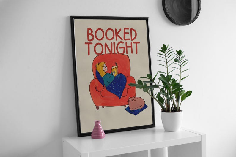 Puede incluir: Impresi&oacute;n art&iacute;stica enmarcada con la frase "BOOKED TONIGHT". La ilustraci&oacute;n muestra a una persona leyendo en un sill&oacute;n rojo, con un gato. Un jarr&oacute;n rosa y una planta en maceta est&aacute;n en una estanter&iacute;a blanca.