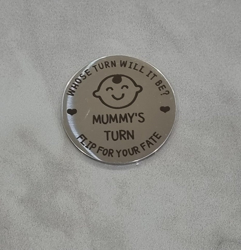 K&ouml;nnte beinhalten: Eine silberne M&uuml;nze mit dem Text "Whose turn will it be?" und "Mummy's turn" mit einer Babygesichtsgrafik und Herzen. Der Text "Flip for your fate" befindet sich ebenfalls auf der M&uuml;nze.