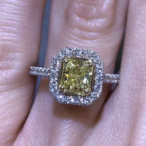 May include: A yellow diamond engagement ring with a double halo setting. The ring is set in white gold and features a large, radiant-cut yellow diamond in the center.