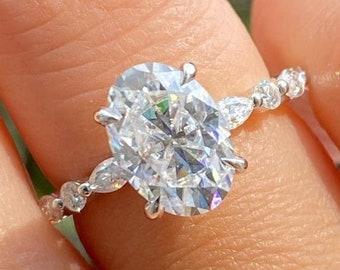 May include: A silver engagement ring with a large oval-shaped diamond and smaller pear-shaped diamonds on the band.