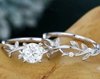 May include: A delicate silver ring set with a large, round, clear gemstone. The band is adorned with a delicate vine design with small leaves and a few tiny gemstones.