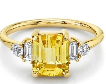 May include: A gold ring with a yellow emerald-cut gemstone and two smaller white diamonds on either side.
