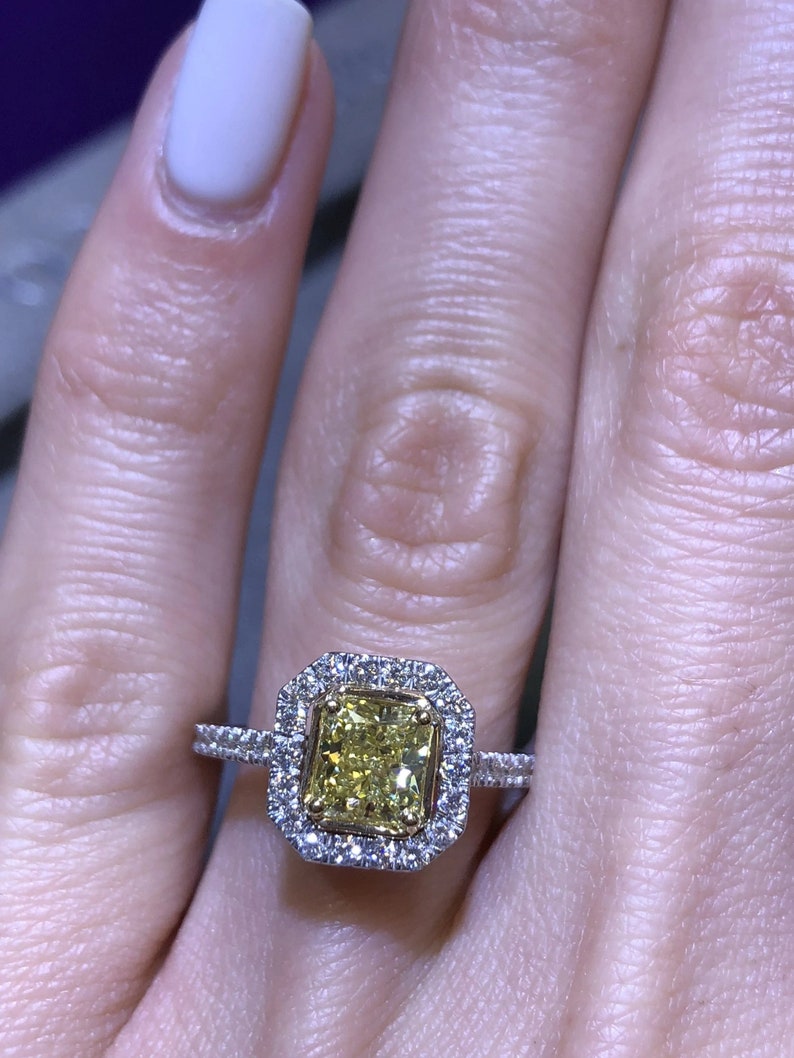 May include: A yellow diamond engagement ring with a double halo setting. The ring is set in white gold and features a large, radiant-cut yellow diamond in the center.