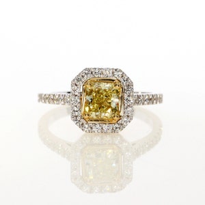 May include: A yellow diamond engagement ring with a square-shaped center stone surrounded by a halo of smaller diamonds. The ring is set in white gold and has a band of smaller diamonds.