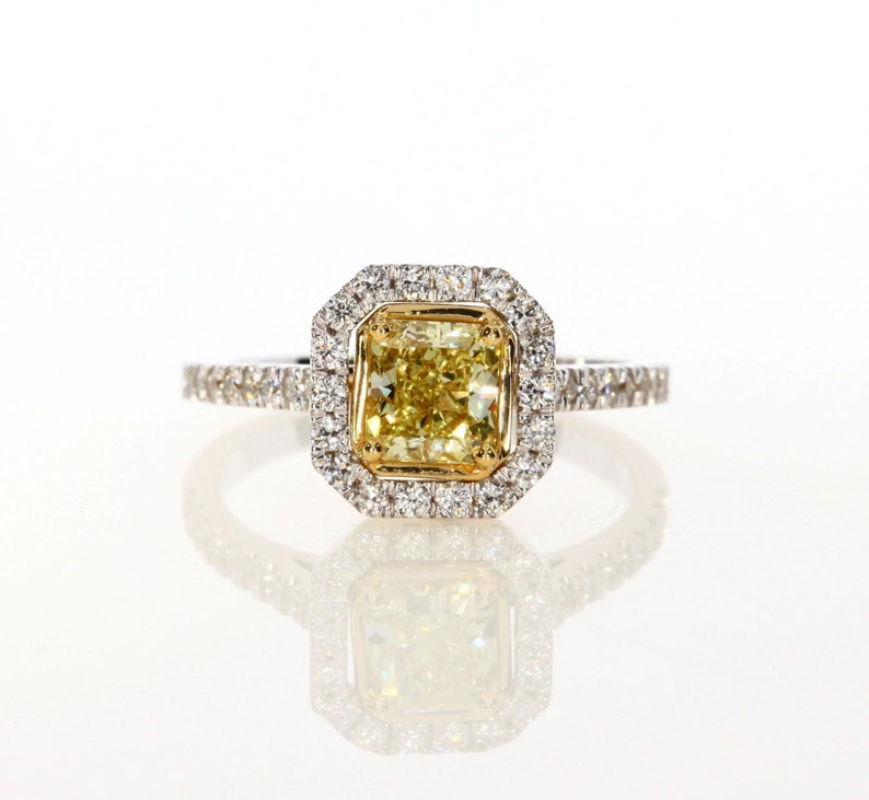 May include: A yellow diamond engagement ring with a square-shaped center stone surrounded by a halo of smaller diamonds. The ring is set in white gold and has a band of smaller diamonds.